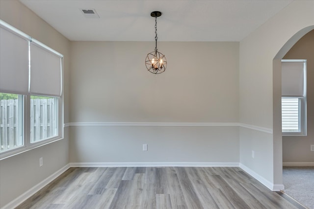 spare room featuring a notable chandelier, arched walkways, baseboards, wood finished floors, and visible vents