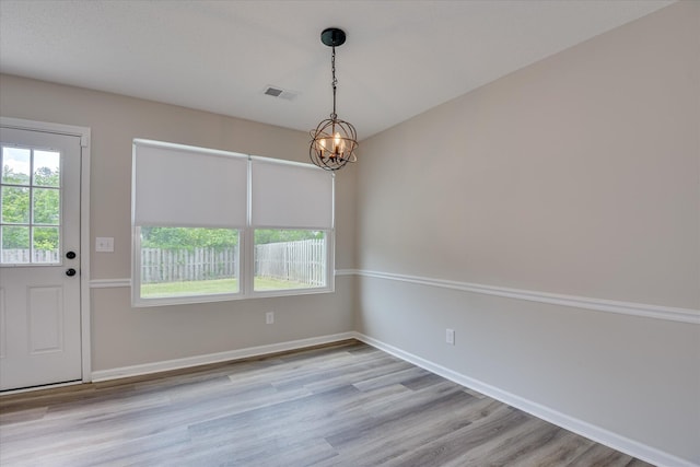 unfurnished dining area with visible vents, baseboards, wood finished floors, and an inviting chandelier