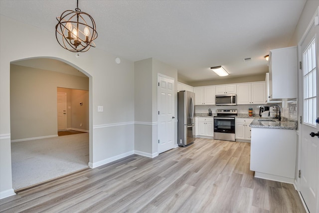 kitchen featuring arched walkways, appliances with stainless steel finishes, a sink, and light wood-type flooring