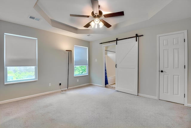 unfurnished bedroom with carpet floors, baseboards, a barn door, and visible vents