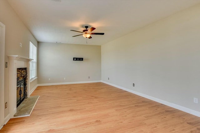 unfurnished living room featuring ceiling fan, a fireplace, baseboards, and light wood-style floors