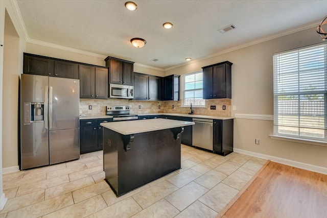 kitchen with crown molding, light countertops, decorative backsplash, appliances with stainless steel finishes, and a kitchen island