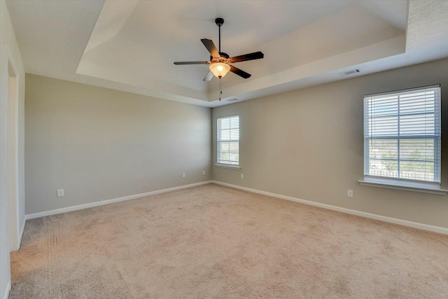 empty room featuring light carpet, visible vents, a tray ceiling, and baseboards