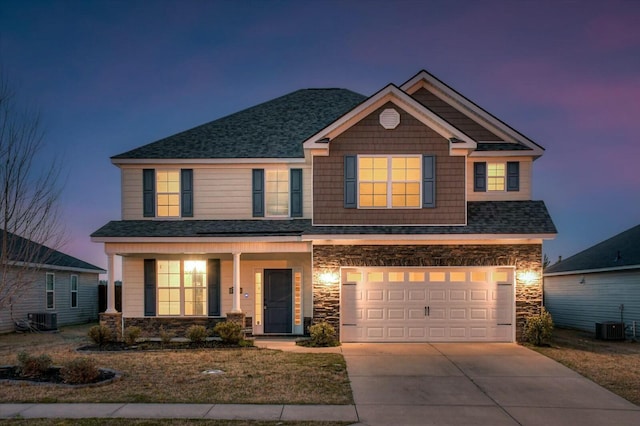 view of front of property with stone siding, an attached garage, central AC, and driveway