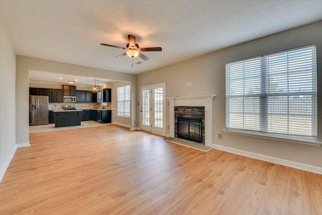 unfurnished living room with a ceiling fan, baseboards, a fireplace, and light wood finished floors