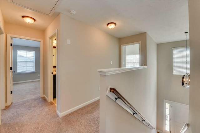 corridor with light carpet, baseboards, and an upstairs landing