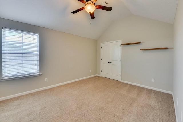 empty room with lofted ceiling, ceiling fan, light colored carpet, visible vents, and baseboards