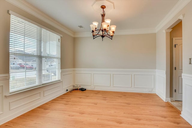 spare room featuring ornamental molding, light wood-type flooring, wainscoting, and a notable chandelier