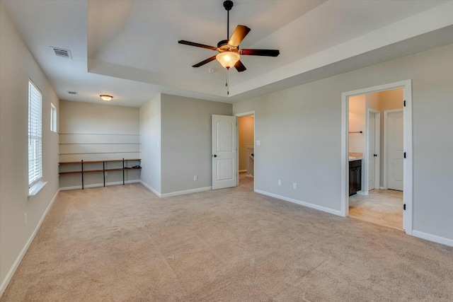 unfurnished bedroom with baseboards, a raised ceiling, visible vents, and light colored carpet