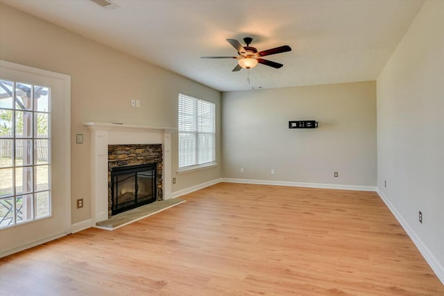 unfurnished living room with baseboards, a stone fireplace, light wood-style flooring, and a ceiling fan