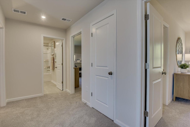 corridor featuring visible vents, baseboards, and light colored carpet