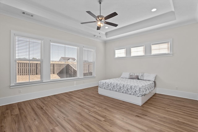 bedroom featuring visible vents, baseboards, a tray ceiling, and wood finished floors