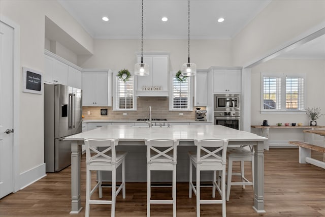 kitchen featuring white cabinetry, backsplash, a kitchen island with sink, and appliances with stainless steel finishes