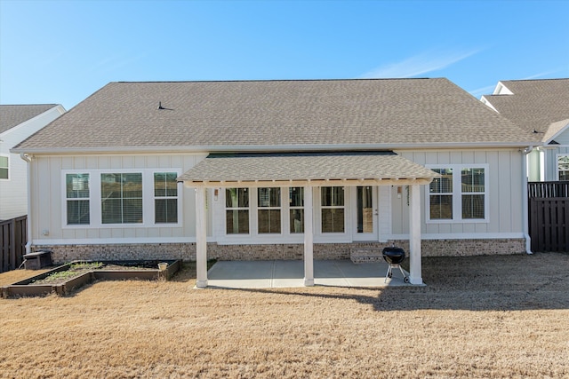 rear view of property featuring a patio area, a shingled roof, a vegetable garden, and fence