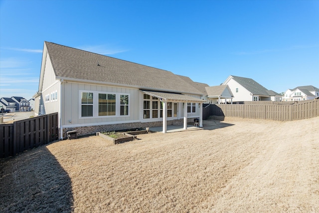 rear view of property with a patio area, board and batten siding, a fenced backyard, and a shingled roof