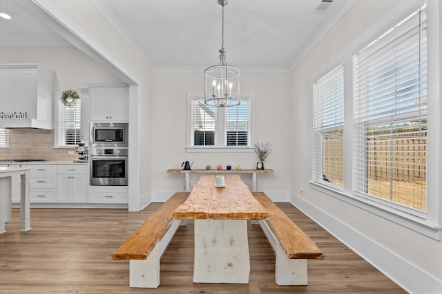 unfurnished dining area featuring a notable chandelier, baseboards, light wood-style floors, and crown molding