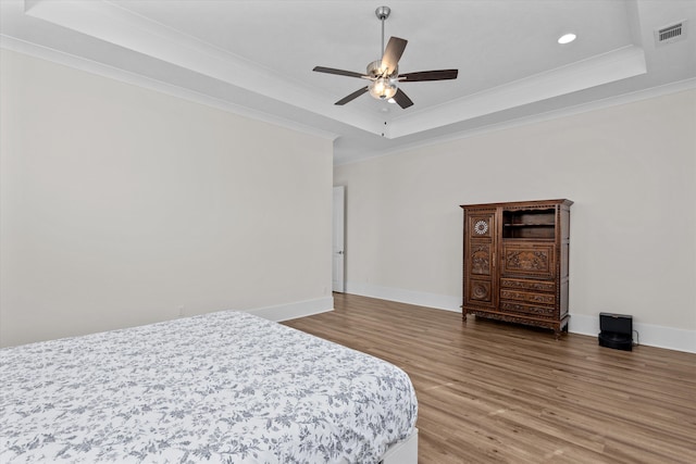 bedroom featuring a tray ceiling, wood finished floors, visible vents, and ornamental molding