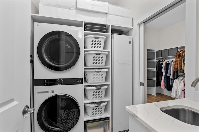 laundry room featuring laundry area, stacked washer / dryer, wood finished floors, and a sink