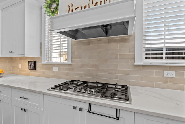 kitchen featuring ventilation hood, decorative backsplash, stainless steel gas stovetop, and white cabinetry