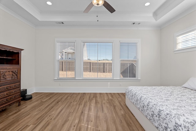 bedroom with a tray ceiling, visible vents, and light wood-style flooring