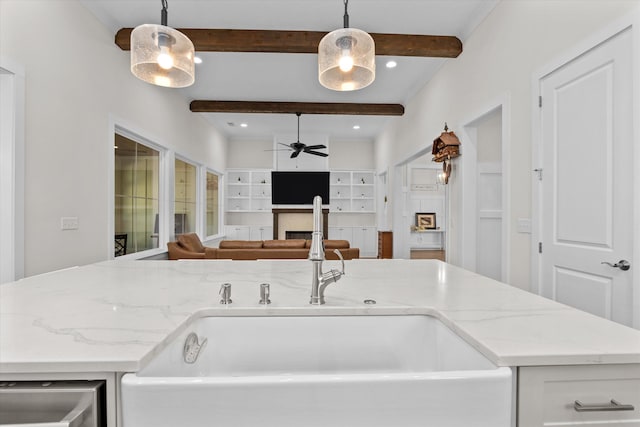 kitchen featuring light stone counters, beam ceiling, a fireplace, and a ceiling fan