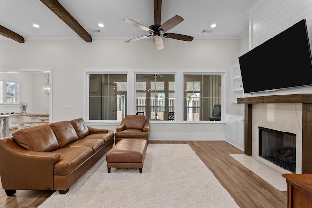 living room featuring a premium fireplace, visible vents, beam ceiling, and wood finished floors