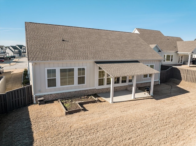 rear view of property featuring a fenced backyard, a vegetable garden, a patio, and roof with shingles