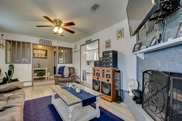 living room featuring ceiling fan, a large fireplace, and light hardwood / wood-style floors