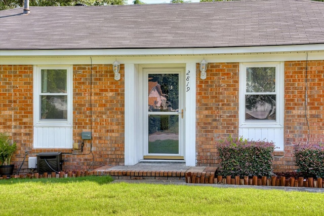 view of exterior entry with a yard and central AC unit