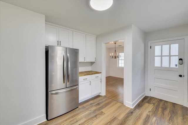 kitchen featuring light hardwood / wood-style flooring, stainless steel fridge, butcher block countertops, a notable chandelier, and white cabinetry