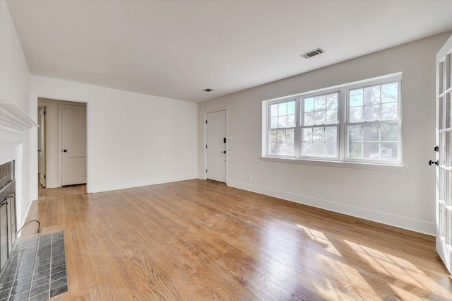 unfurnished living room featuring a tiled fireplace and light wood-type flooring