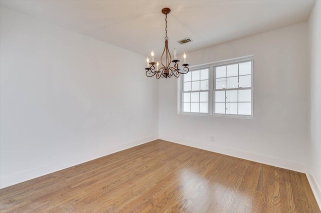 empty room with hardwood / wood-style floors and an inviting chandelier