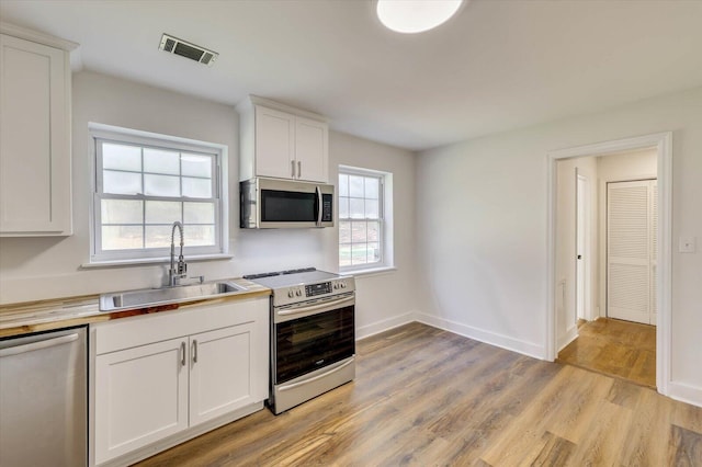 kitchen with sink, white cabinets, light hardwood / wood-style flooring, and appliances with stainless steel finishes