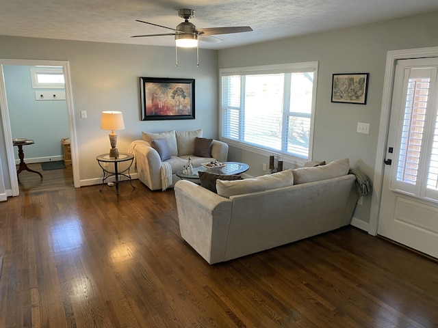 living room featuring dark wood-type flooring, ceiling fan, and a textured ceiling