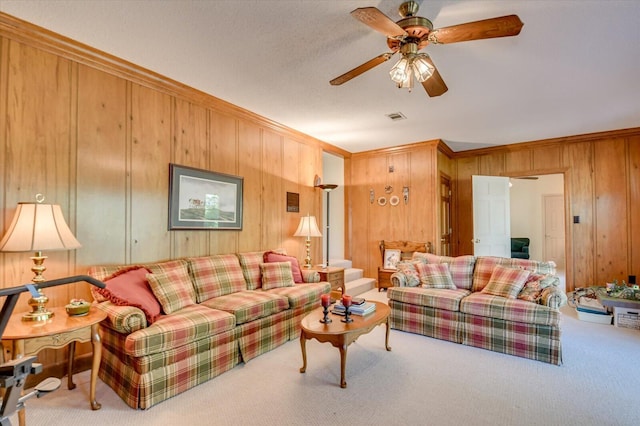 carpeted living area with ceiling fan, ornamental molding, visible vents, and wooden walls
