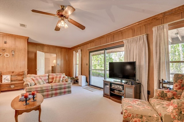 living area featuring wood walls, visible vents, crown molding, carpet flooring, and ceiling fan