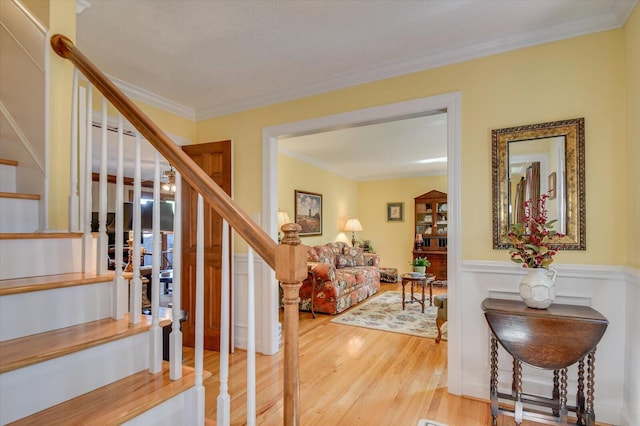 staircase with wainscoting, wood finished floors, and crown molding