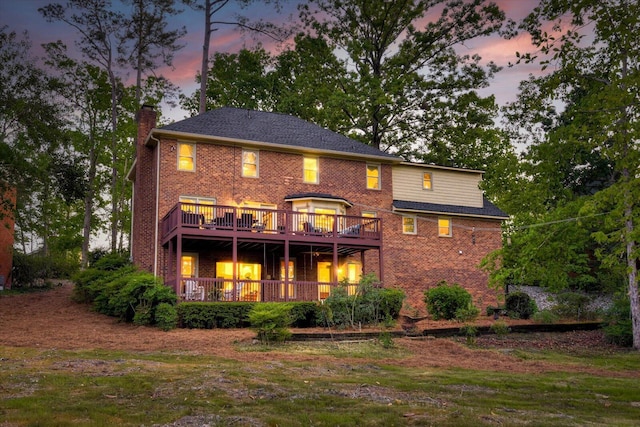 back of property at dusk featuring a chimney, a wooden deck, and brick siding