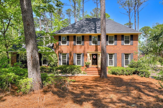 colonial home with brick siding and a shingled roof