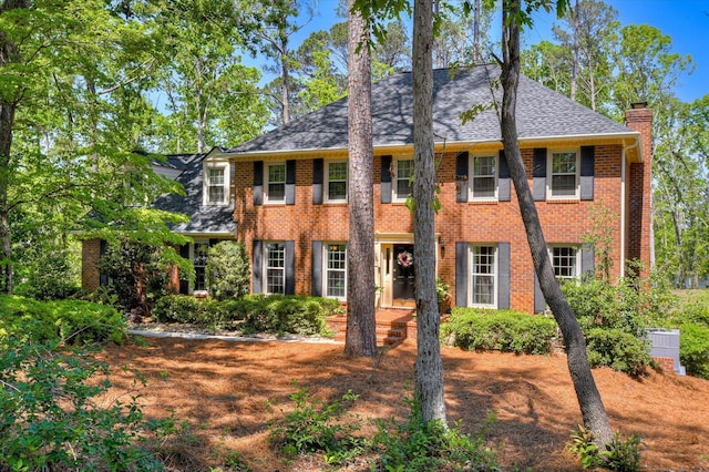 colonial house with a chimney, roof with shingles, and brick siding