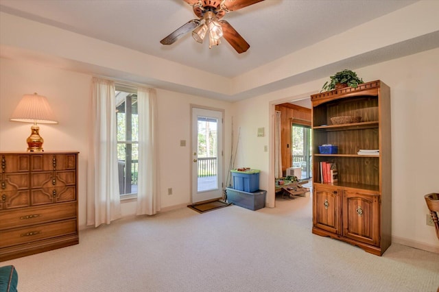 living area with a ceiling fan, baseboards, and light colored carpet