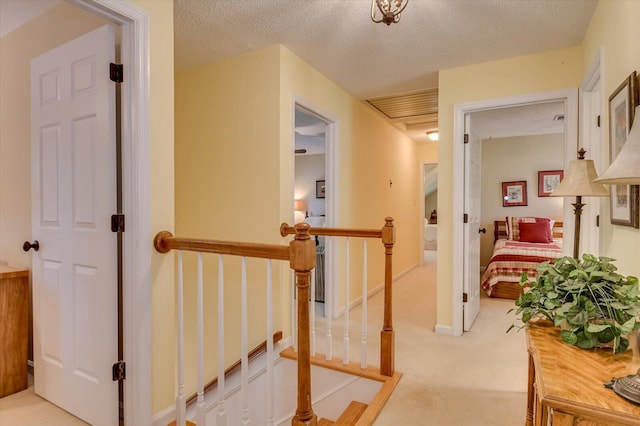 corridor featuring light carpet, a textured ceiling, and an upstairs landing