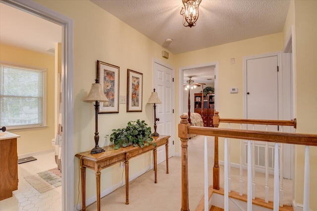 corridor featuring light colored carpet, baseboards, a textured ceiling, and visible vents