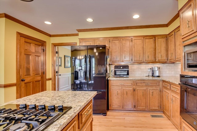 kitchen featuring light wood finished floors, light stone countertops, crown molding, decorative backsplash, and black appliances