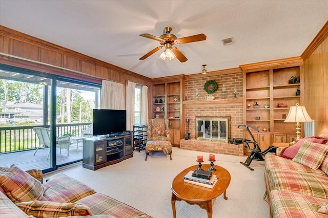 carpeted living room featuring wood walls, visible vents, crown molding, built in shelves, and ceiling fan