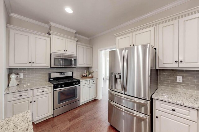 kitchen with ornamental molding, wood finished floors, white cabinets, appliances with stainless steel finishes, and backsplash