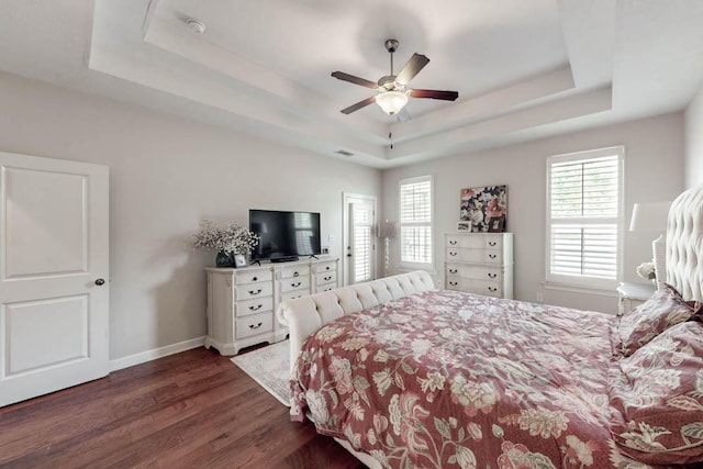 bedroom featuring a tray ceiling, dark wood-style floors, baseboards, and multiple windows