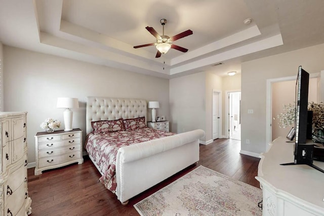 bedroom featuring visible vents, baseboards, dark wood-type flooring, a tray ceiling, and a ceiling fan