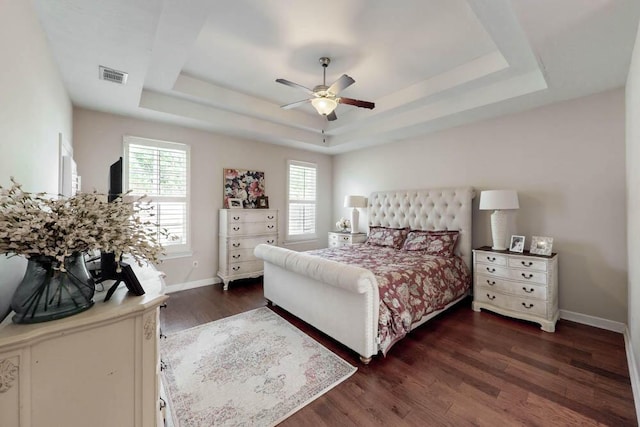 bedroom featuring dark wood-style flooring, a raised ceiling, a ceiling fan, baseboards, and visible vents
