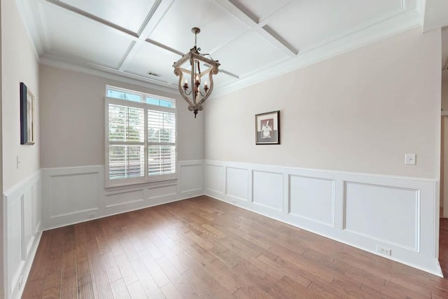 empty room featuring wood-type flooring, coffered ceiling, a wainscoted wall, and a chandelier